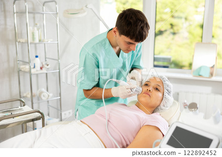 Young male cosmetologist doing whitening procedure to young woman 122892452