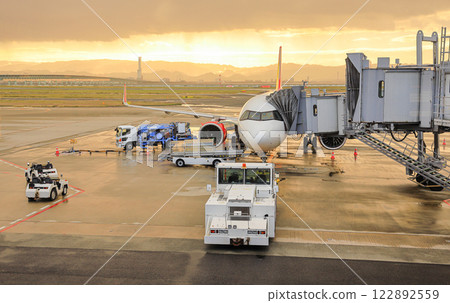 Airport baggage tug (baggage dolly transport) on duty and Ground Service fuel truck Refueling an aircraft at aircraft bay. Airport baggage tug (baggage dolly transport) on duty and Ground Service fuel truck Refueling an aircraft at aircraft bay. 122892559