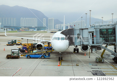 Airport baggage tug (baggage dolly transport) on duty and Ground Service fuel truck Refueling an aircraft at aircraft bay. Airport baggage tug (baggage dolly transport) on duty and Ground Service fuel truck Refueling an aircraft at aircraft bay. 122892562