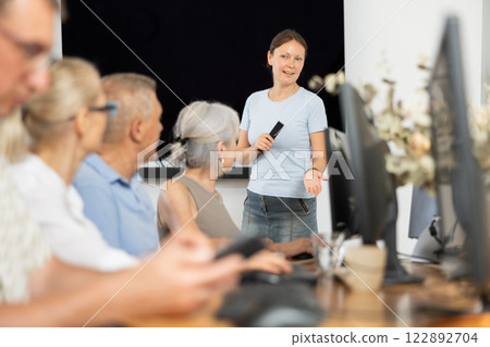 Middle-aged woman teacher speaking to mature attendees of computer courses 122892704