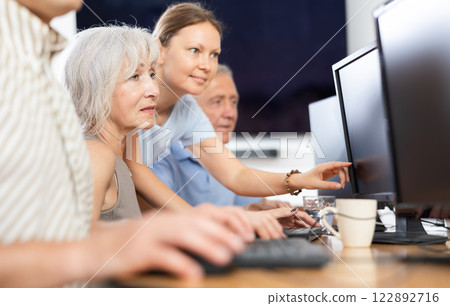 Old woman learning computer programs with teacher in training room 122892716