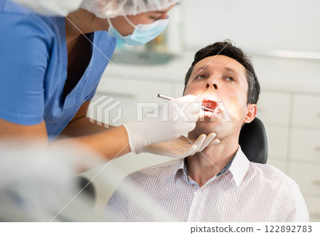 Young female dentist examining male patient Young female dentist examining male patient 122892783
