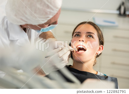Mature man doctor dentist in white coat examines oral cavity of girl patient in dentistry. Mature man doctor dentist in white coat examines oral cavity of girl patient in dentistry. 122892791