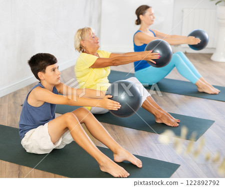 Preteen boy practicing seated fitness pose with softball in hands in training room 122892792