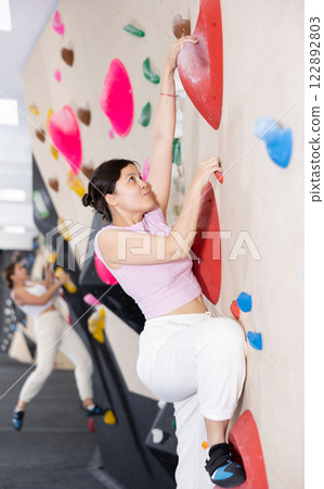 Sporty woman climbing on bouldering wall demonstrating physical strength, technical skill, and determination Sporty woman climbing on bouldering wall demonstrating physical strength, technical skill, and determination 122892803