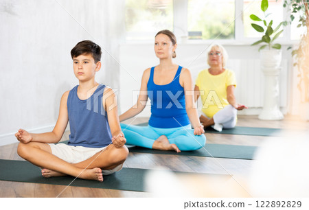 Preteen boy practicing half lotus pose of yoga in light fitness room 122892829