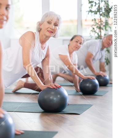 Mature and young lady is on all fours and put one palm on soft ball. Close-up 122892855