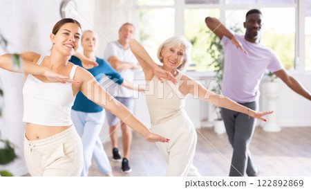 Female instructor teaches mature students of dance class basic movements of hip hop dance Female instructor teaches mature students of dance class basic movements of hip hop dance 122892869