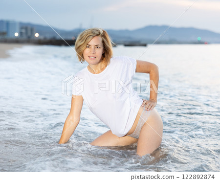 Lovely woman posing on sandy beach in sea waves Lovely woman posing on sandy beach in sea waves 122892874
