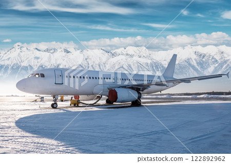 White passenger airliner on the airport apron at winter on the background of high picturesque mountains White passenger airliner on the airport apron at winter on the background of high picturesque mountains 122892962
