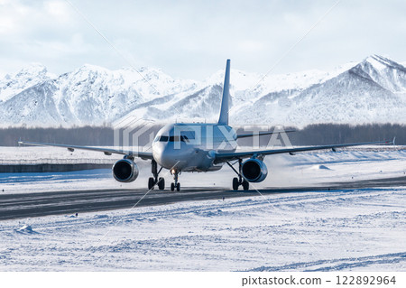 White passenger jet plane taxiing on taxiway in snowy winter day on the background of high snow capped mountains White passenger jet plane taxiing on taxiway in snowy winter day on the background of high snow capped mountains 122892964