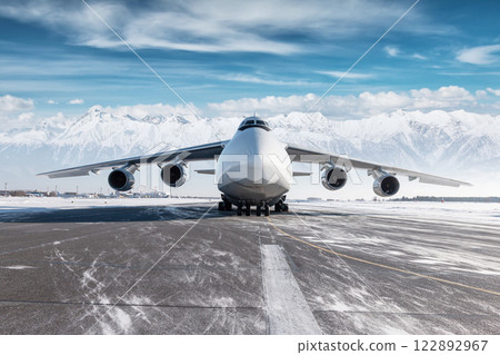 Front view of the white wide body transport cargo aircraft at winter airport on the background of high scenic mountains Front view of the white wide body transport cargo aircraft at winter airport on the background of high scenic mountains 122892967