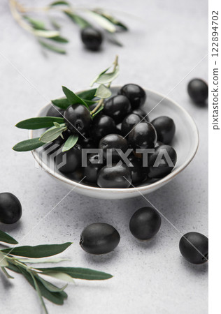 Black olives with olive branches served in ceramic bowl on gray background Black olives with olive branches served in ceramic bowl on gray background 122894702