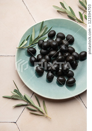 Black olives served on ceramic plate with olive branches on tiled surface Black olives served on ceramic plate with olive branches on tiled surface 122894703