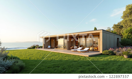 Modern coastal house with large windows and outdoor lounge area overlooking the sea at sunset 122897337