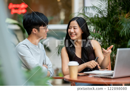 A cheerful Asian woman enjoys sharing her ideas with her colleague during an informal meeting. A cheerful Asian woman enjoys sharing her ideas with her colleague during an informal meeting. 122898080