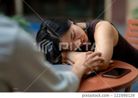 A tired Asian woman takes a nap at an outdoor table while working on her tasks. 122898126