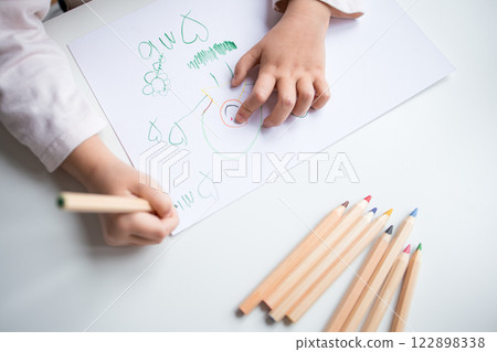 Child drawing with colored pencils on white paper 122898338