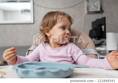 A curious toddler distracted during mealtime, observing surroundings with thoughtful expression. A curious toddler distracted during mealtime, observing surroundings with thoughtful expression. 122898341