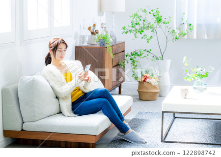 Woman sitting on a sofa and looking at a smartphone Woman sitting on a sofa and looking at a smartphone 122898742