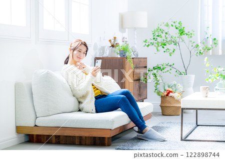 Woman sitting on a sofa and looking at a smartphone 122898744