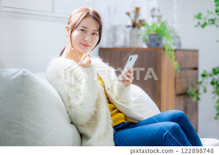 Woman sitting on a sofa and looking at a smartphone 122898748