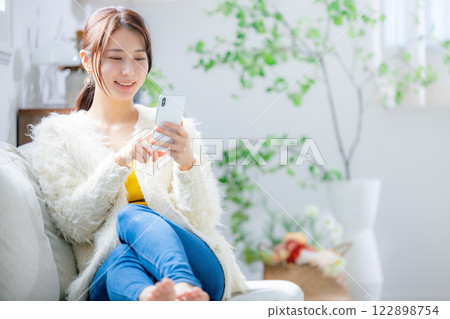 Woman sitting on a sofa and looking at a smartphone 122898754