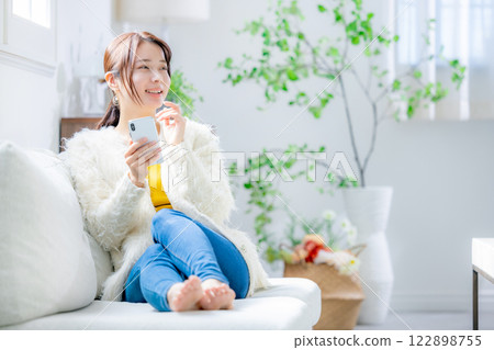 Woman sitting on a sofa and looking at a smartphone 122898755