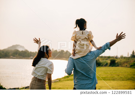 Asian family child girl piggyback riding back on father raising hands like flying outdoor nature park with mother, Happy parent daughter having fun together, Tourist lifestyle family leisure activity Asian family child girl piggyback riding back on father raising hands like flying outdoor nature park with mother, Happy parent daughter having fun together, Tourist lifestyle family leisure activity 122899581