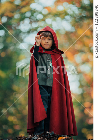 Cute cosplayer hobbit kid in cape costume in forest watching gold ring. Fantasy journey in fairytale Cute cosplayer hobbit kid in cape costume in forest watching gold ring. Fantasy journey in fairytale 122899840