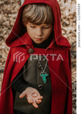 Little cosplayer hobbit boy in cape costume in autumn forest admiring golden ring. Fantasy journey Little cosplayer hobbit boy in cape costume in autumn forest admiring golden ring. Fantasy journey 122899889