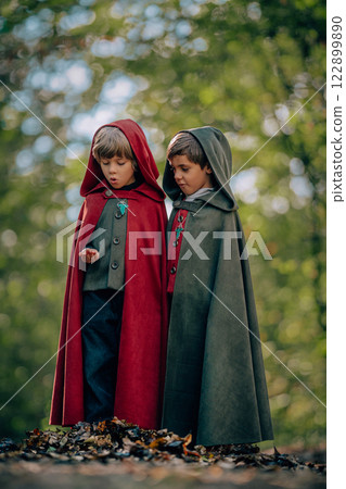 Hobbits boys in cape costumes standing in green forest with ring. Fantasy journey, halloween Hobbits boys in cape costumes standing in green forest with ring. Fantasy journey, halloween 122899890