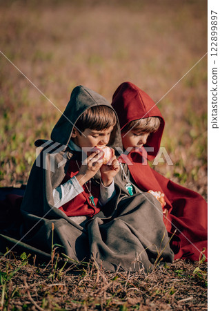 Hobbits boys in costumes sitting on autumn ground to eat apples. Fantasy journey, halloween Hobbits boys in costumes sitting on autumn ground to eat apples. Fantasy journey, halloween 122899897