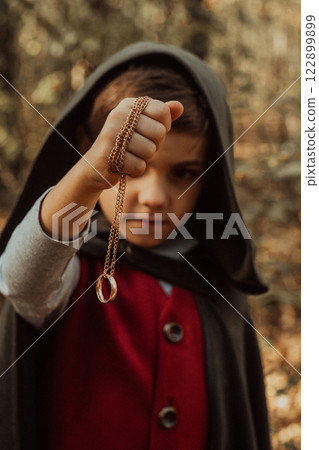 Little cosplayer hobbit boy in cape costume in autumn forest admiring golden ring. Fantasy journey 122899899