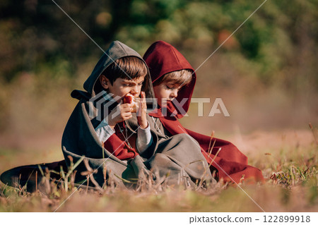 Hobbits boys in costumes sitting on autumn ground to eat apples. Fantasy journey, halloween 122899918