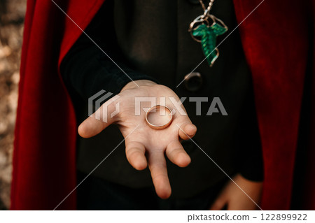 Boy cosplayer in hobbit cape costume holds golden ring. Fantasy journey, halloween, fellowship 122899922