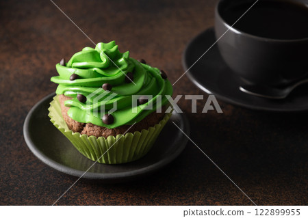 St. Patrick's Day coffee and homemade cupcake with green whipped cream and chocolate sprinkles on brown background. Close up. Festive food, 122899955