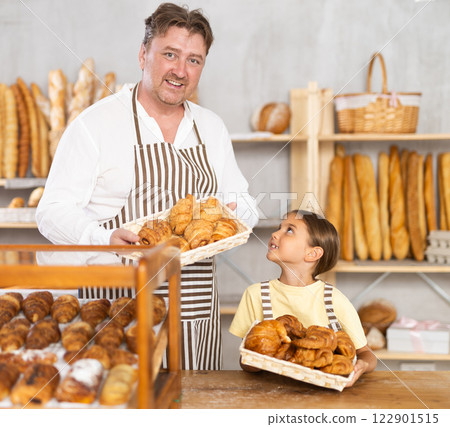 Young daughter helps her father place hot croissants on bakery display. Family business 122901515