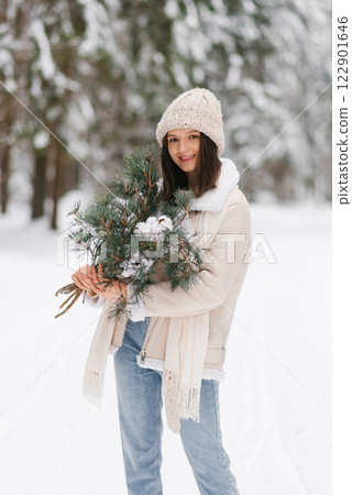 Smiling woman is holding pine tree and cotton in her hand while wearing white hat, jacket. Concept of warmth and coziness Smiling woman is holding pine tree and cotton in her hand while wearing white hat, jacket. Concept of warmth and coziness 122901646