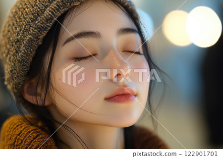 Young asian woman with brown hat and red scarf is sitting with her eyes closed. She has a calm and peaceful expression on her face 122901701