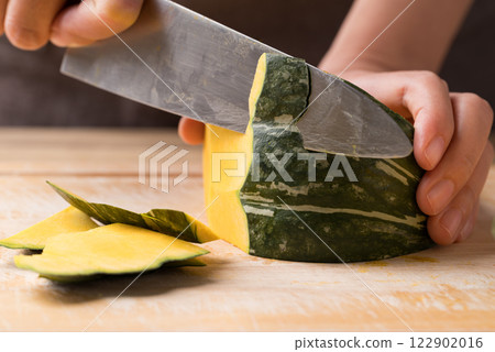 Hand holding kitchen knife and cutting green pumpkin on wooden board, Homemade cooking 122902016