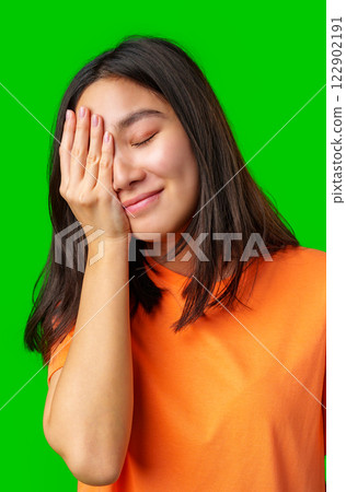 Young woman smiling with one hand on her face against a bright green background during a lighthearted moment Young woman smiling with one hand on her face against a bright green background during a lighthearted moment 122902191