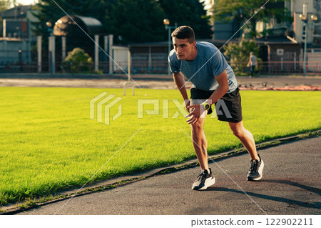Man practicing sprinting on a track in an outdoor athletic facility during late afternoon Man practicing sprinting on a track in an outdoor athletic facility during late afternoon 122902211