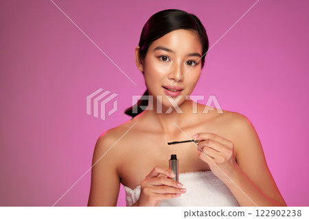 Model demonstrating mascara application against a vibrant pink background during a beauty tutorial session 122902238