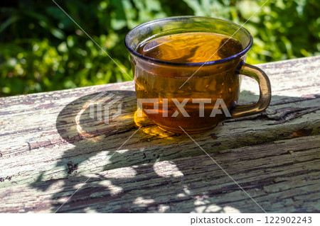 Transparent cup of tea and shadows from plants on wooden bench in garden on sunny summer afternoon. Simple, slow life 122902243