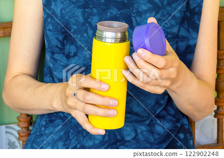 Yellow thermos with violet cap in woman's hands. Close-up, unrecognizable person Yellow thermos with violet cap in woman's hands. Close-up, unrecognizable person 122902248