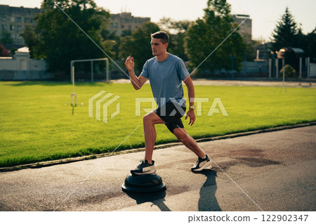 Young man performs outdoor balance training on a stability disc during late afternoon at a city park 122902347
