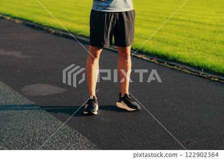Athletic individual preparing for a workout on a sunny day at a park track with vibrant grass and black pavement 122902364
