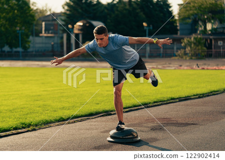 Man practicing balance on a stability board at an outdoor sports facility during daylight hours Man practicing balance on a stability board at an outdoor sports facility during daylight hours 122902414