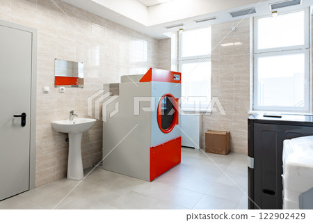 Modern laundry area featuring a red and gray washing machine in a bright, clean environment with natural light filtering through windows 122902429